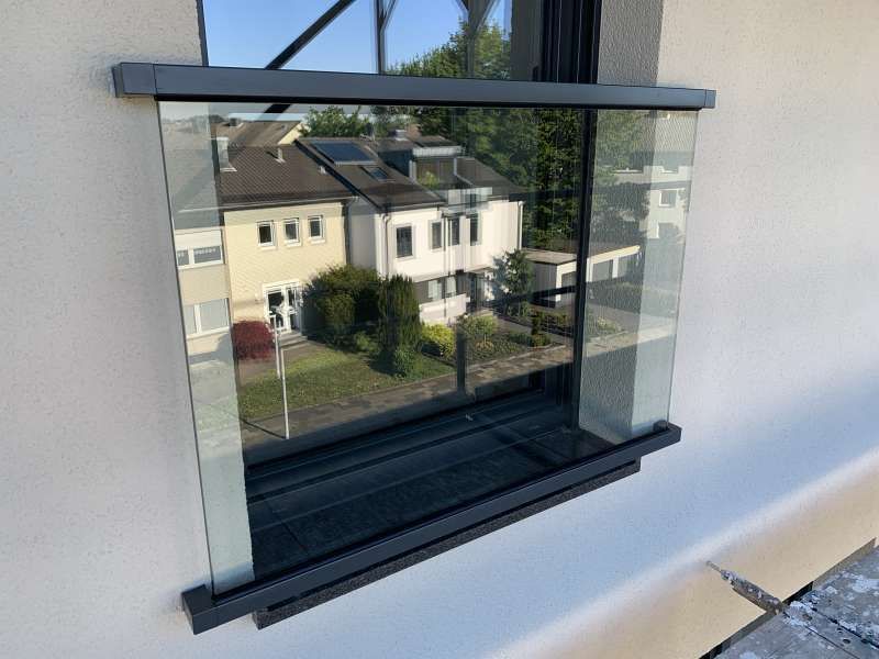 Ein Fenster mit einem Glasgeländer an der Seite eines Gebäudes.