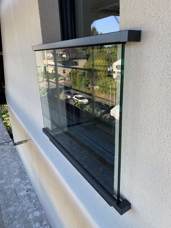Ein Fenster mit einem Glasgeländer an der Seite eines Gebäudes.