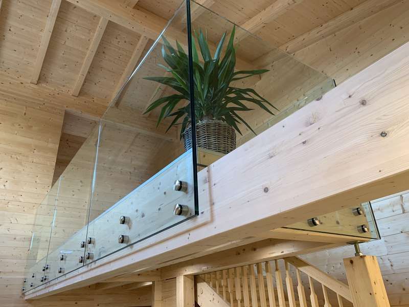 Eine Holztreppe mit Glasgeländer und einer Topfpflanze auf dem Geländer.