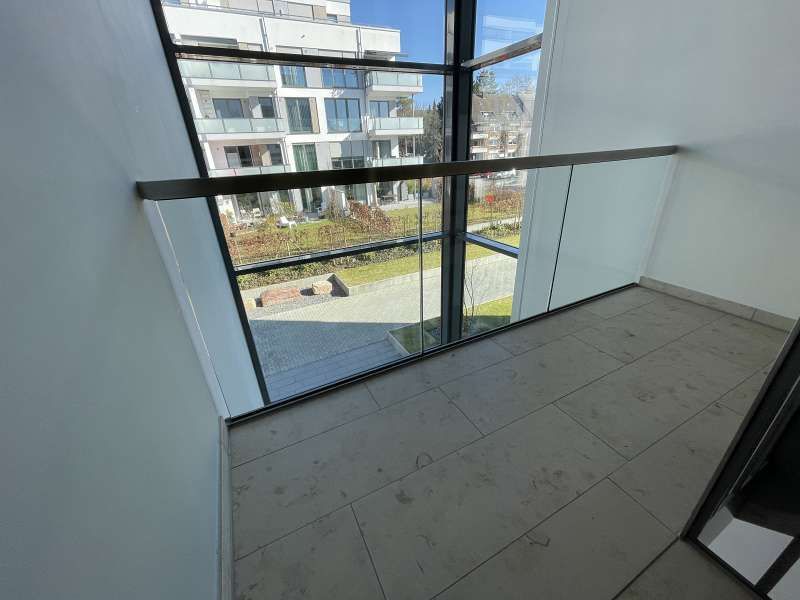 Ein Balkon mit Glasgeländer und Blick auf ein Gebäude.