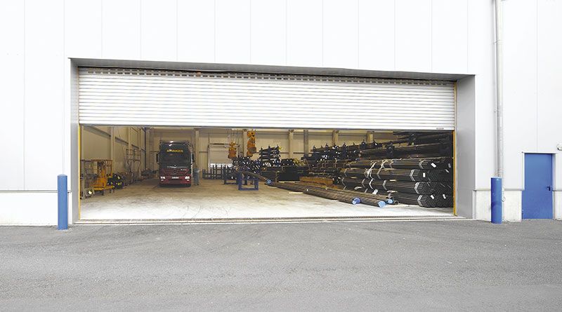 Ein roter Gabelstapler steht in einer Lagerhalle, das große Garagentor ist geöffnet.