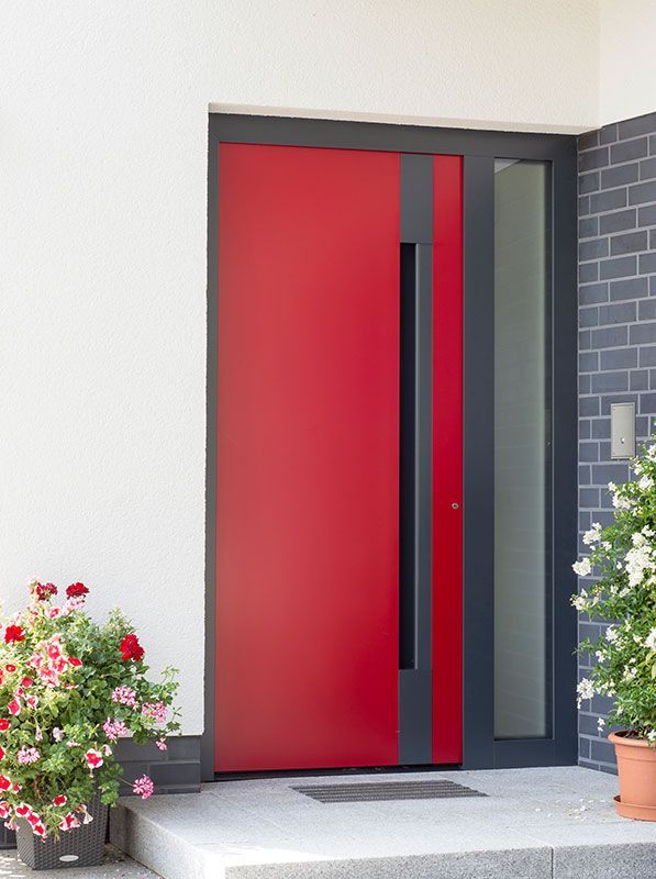 Eine rote Tür mit schwarzem Rahmen steht auf einer Veranda neben einer Topfpflanze.