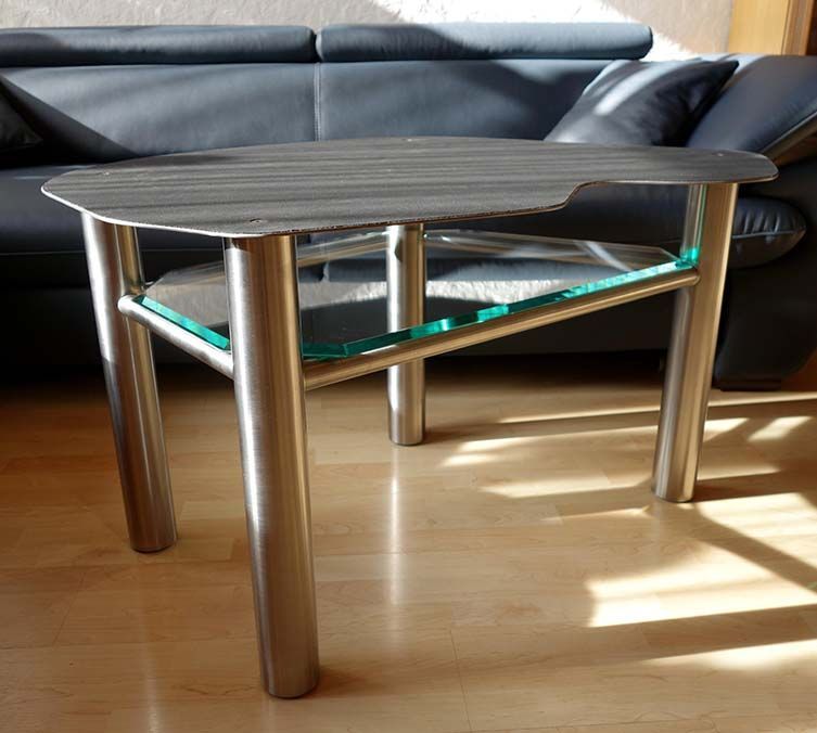 Ein Couchtisch mit Glasablage steht vor einer schwarzen Ledercouch