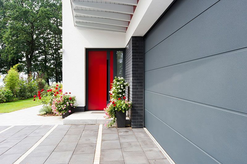 Ein modernes Haus mit einer roten Tür und einem grauen Garagentor.