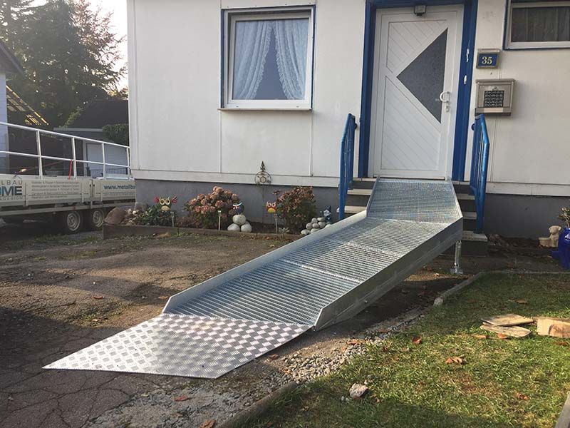 Vor einem weißen Haus steht eine Metallrampe.