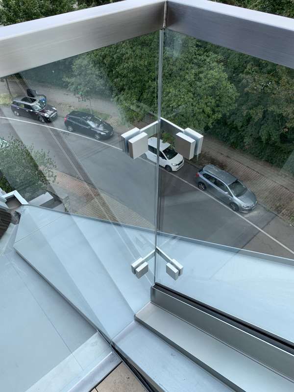 Ein Balkon mit einem Glasgeländer und einer Spiegelung von Autos im Glas.