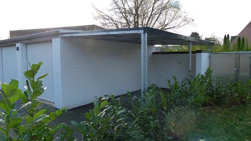 Eine weiße Garage mit einem Vordach ist von Büschen umgeben.