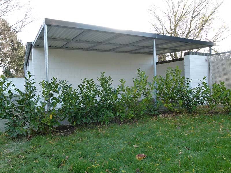 Ein weißes Gebäude mit einem Metalldach ist von Büschen und Gras umgeben