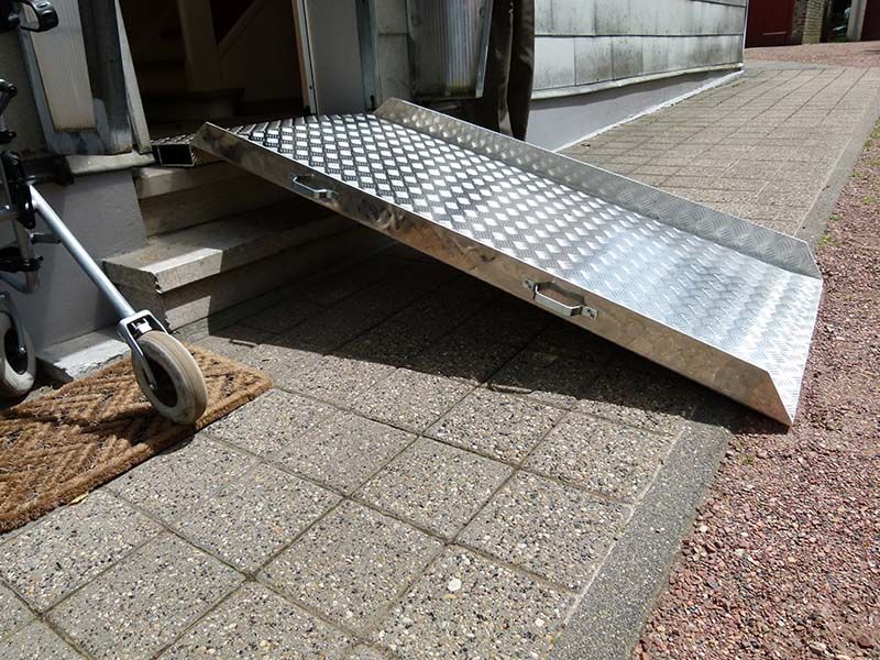 Auf dem Bürgersteig steht neben einem Rollstuhl eine Metallrampe.