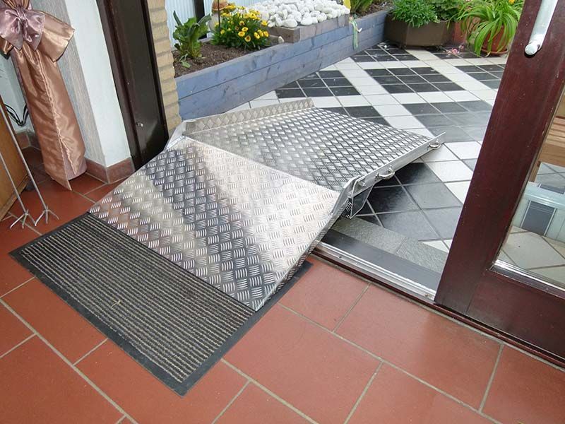 Auf einem gefliesten Boden neben einer Tür steht eine Metallrampe.