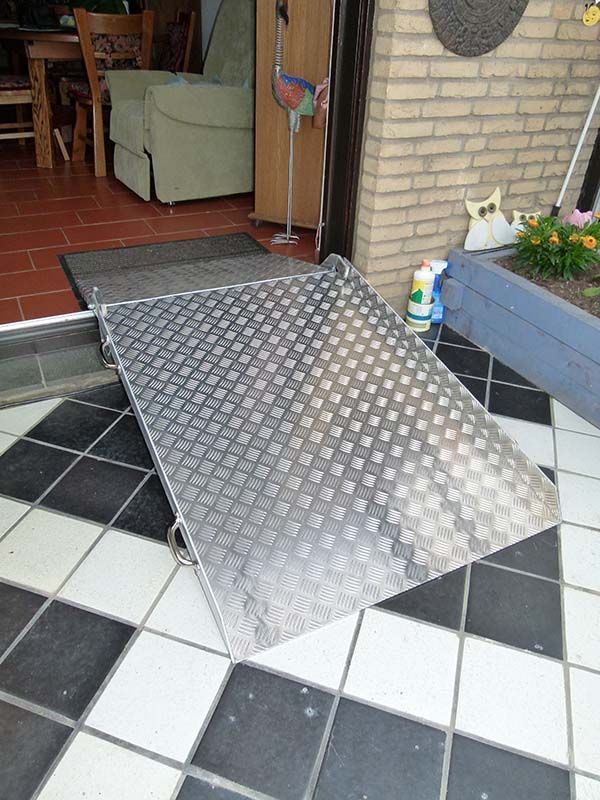 Auf einem gefliesten Boden vor einer Tür steht eine Metallrampe.