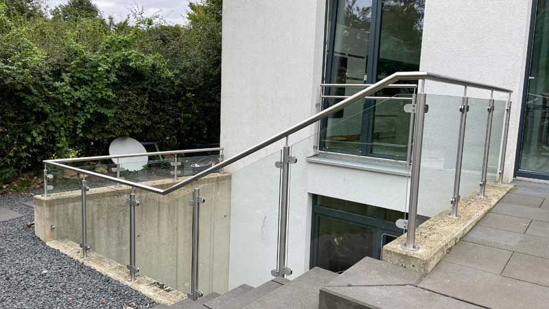 Eine Treppe mit Edelstahlgeländer und Glasgeländer, die in einen Keller führt.