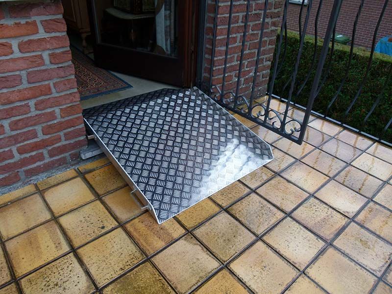 Auf einem gefliesten Boden vor einem Backsteingebäude steht eine Metallrampe.