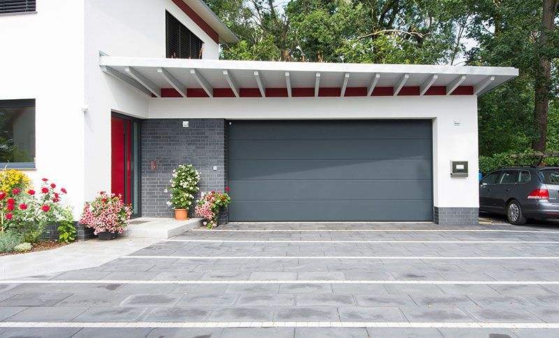 Ein weißes Haus mit einem grauen Garagentor und einem davor geparkten Auto.