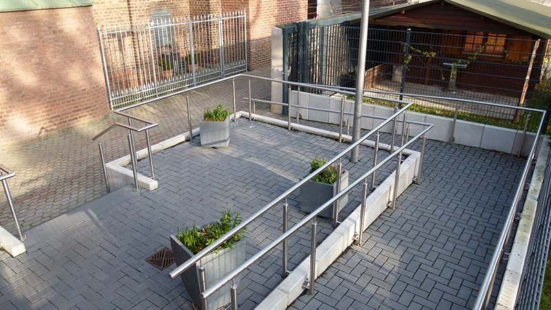 Ein Ziegelweg mit Edelstahlgeländer und Pflanzkübeln.