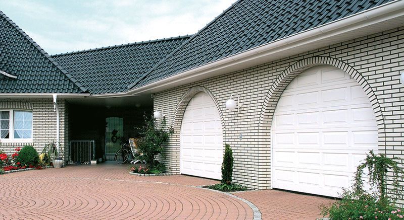Ein weißes Backsteinhaus mit blauem Dach und zwei weißen Garagentoren