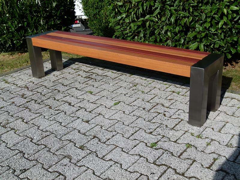 Auf einem gepflasterten Gehweg steht eine Holzbank.