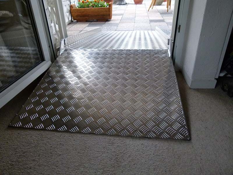 Eine Metallrampe, die zu einer Tür führt, im Hintergrund ein Blumentopf