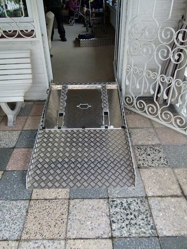 Auf einem gefliesten Boden vor einer Tür steht eine Metallrampe.