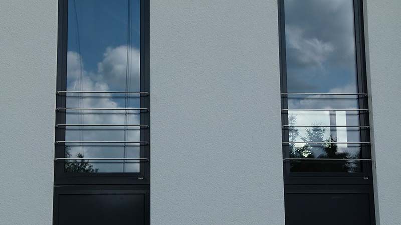 Zwei Fenster an einem weißen Gebäude, in denen sich Wolken spiegeln