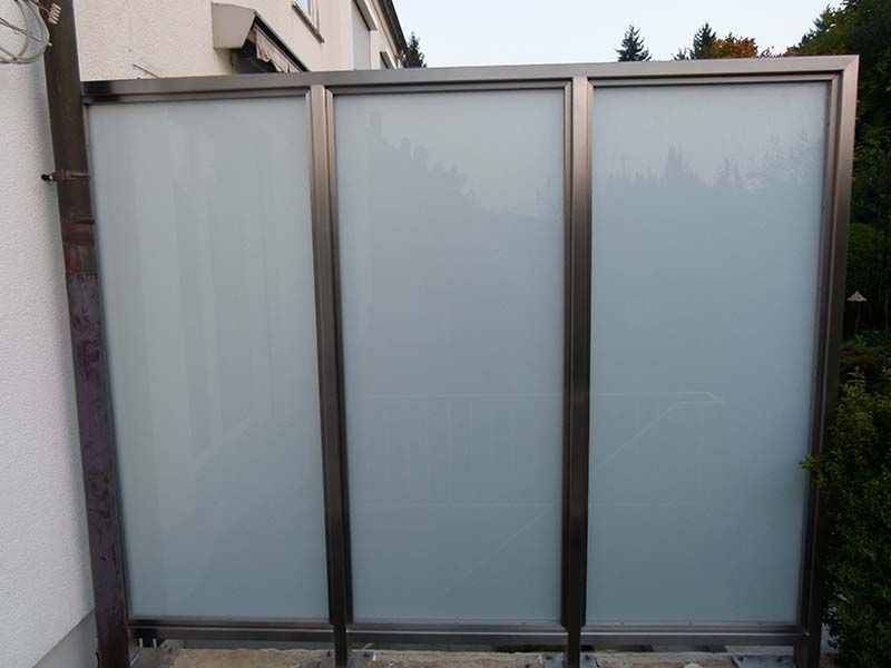 Vor einem Haus steht ein Zaun aus Edelstahl und Milchglas.