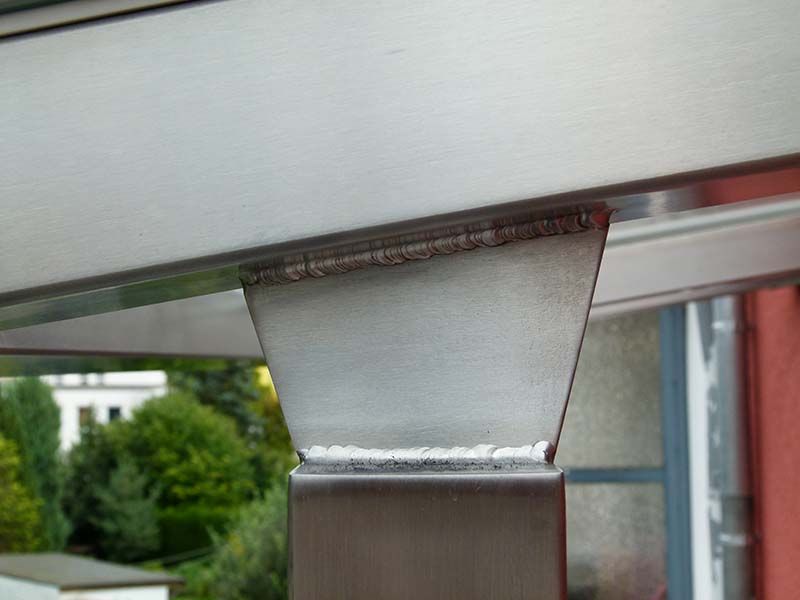 Eine Nahaufnahme eines Edelstahlpfostens mit einem Fenster im Hintergrund