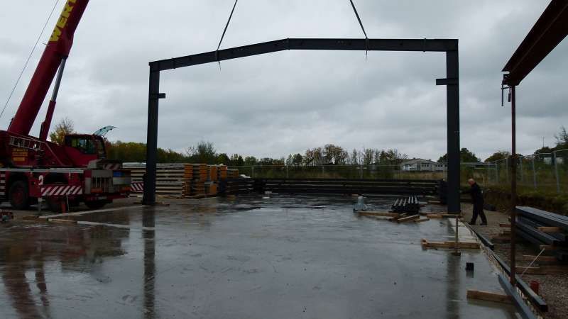 Ein roter Kran hebt auf einem Parkplatz eine große Metallkonstruktion an.