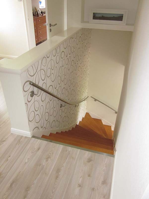 Eine Holztreppe mit weißem Geländer und gemusterter Wand.