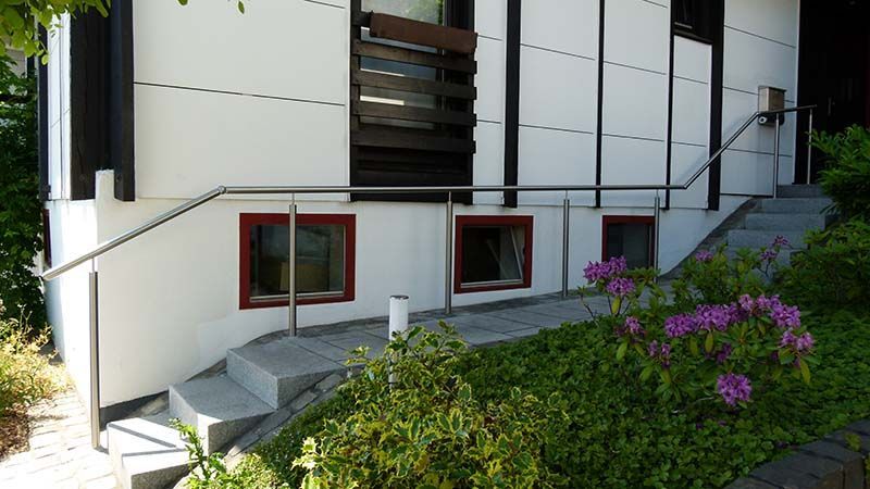 Ein weißes Haus mit einer Treppe hinauf und einem Geländer aus Edelstahl.