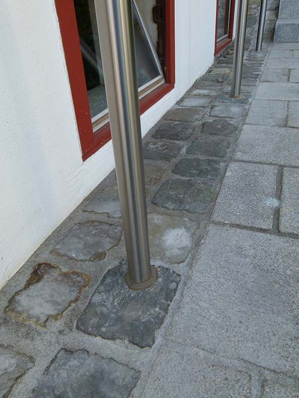 Ein Edelstahlmast steht auf einem Gehweg neben einem Gebäude