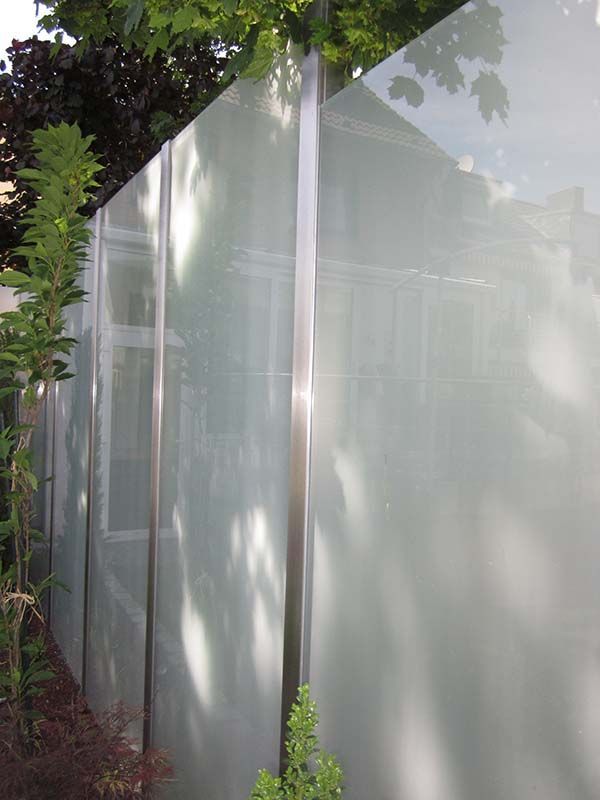 Ein Zaun aus Glas und Edelstahl mit Bäumen im Hintergrund