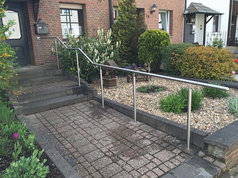 Ein gemauerter Gehweg mit Edelstahlgeländer vor einem Haus.