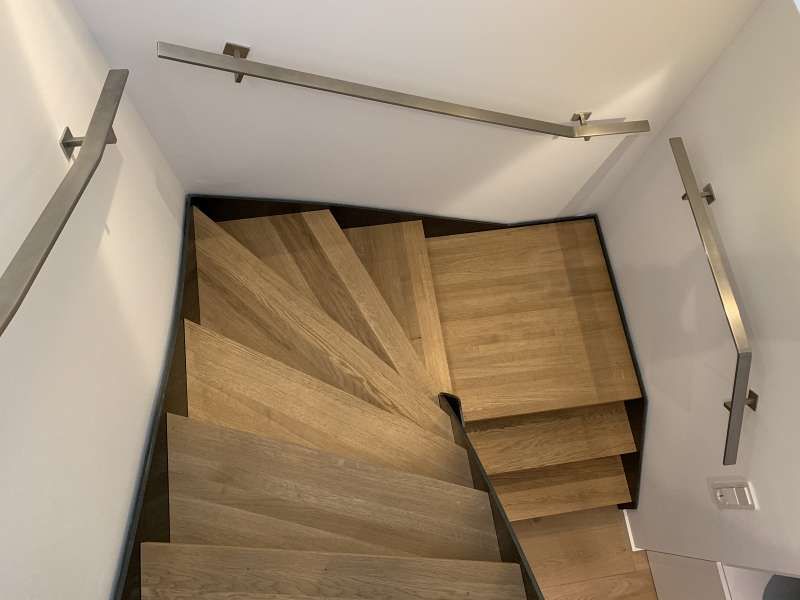 Eine Holztreppe mit Metallgeländer und einer weißen Wand.