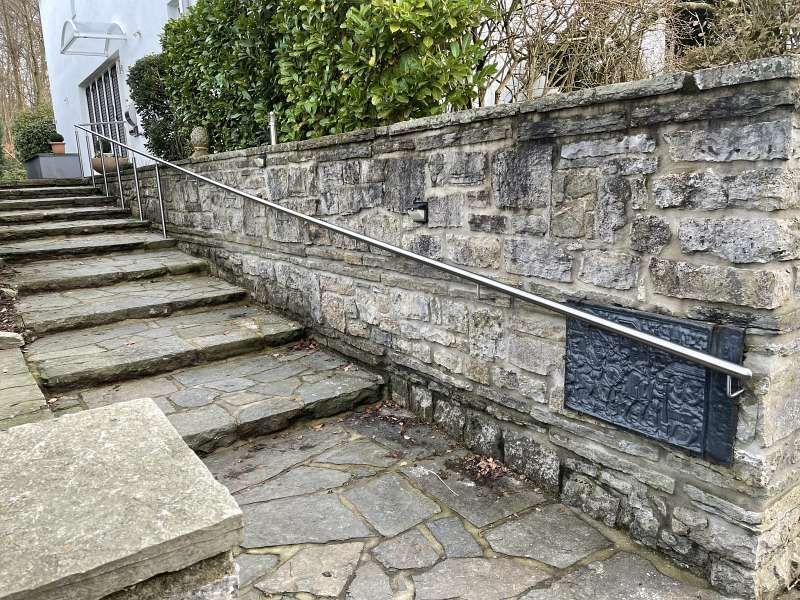Eine Treppe, die zu einer Steinmauer mit Metallgeländer hinaufführt.