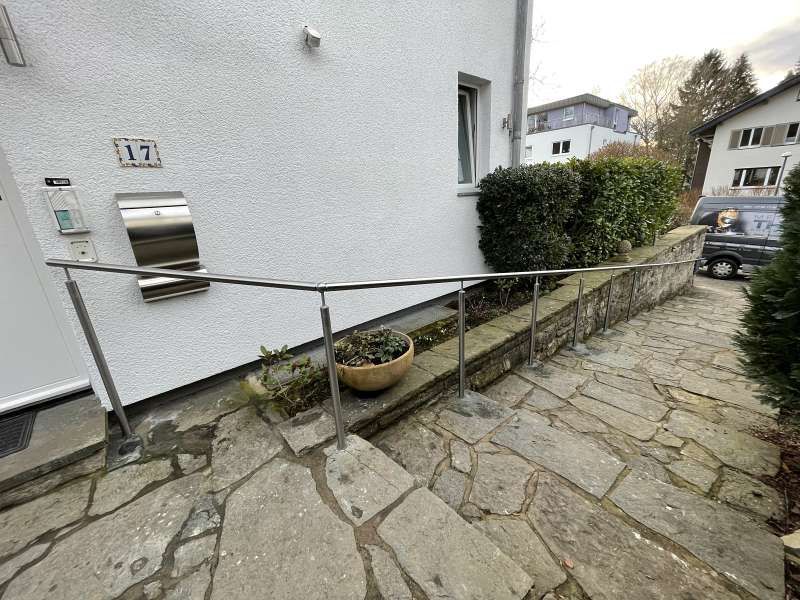 Ein Steinweg führt zu einem weißen Haus mit einem Metallgeländer.