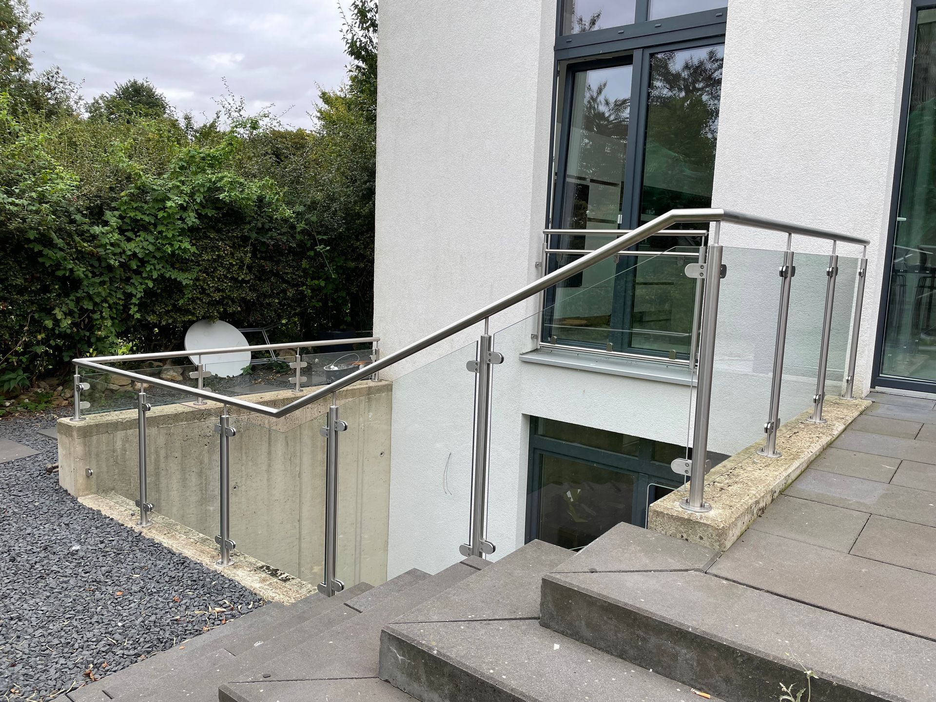 Außentreppe mit Metall- und Glasgeländer, die zu einer tiefer gelegenen Ebene des Gebäudes hinunterführt.