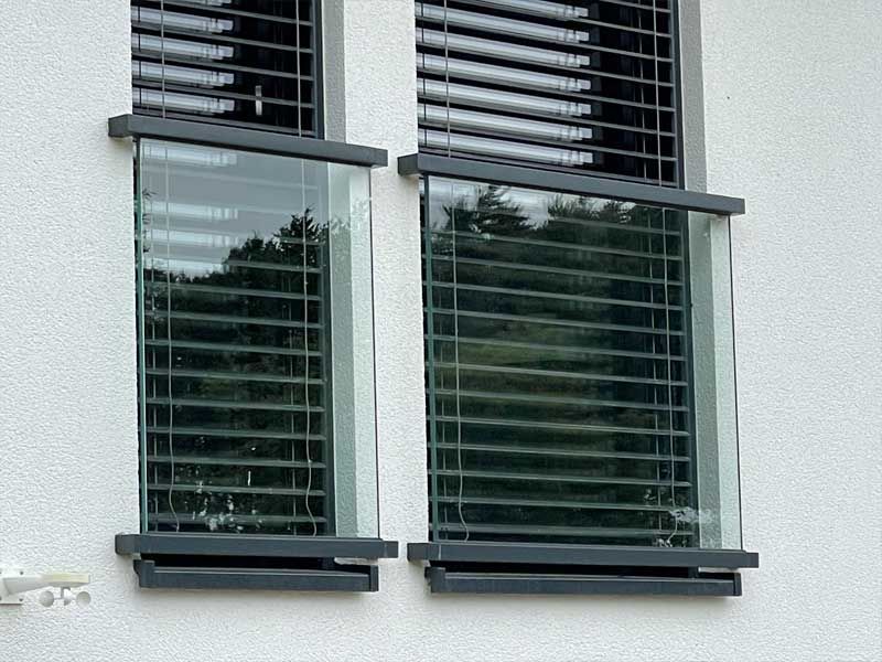 Ein weißes Gebäude mit zwei Fenstern mit Jalousien.