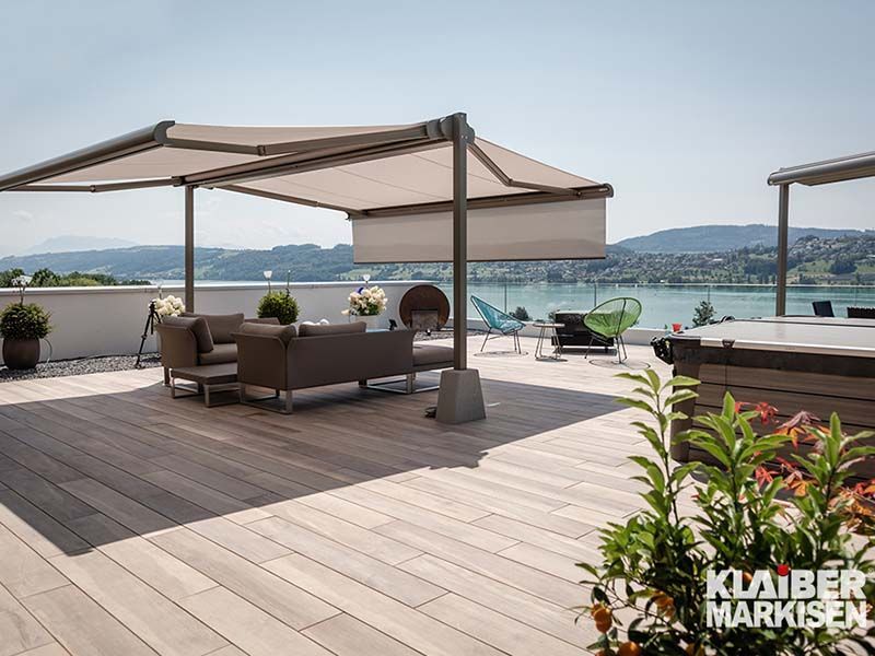 Eine Terrasse mit Sofa, Tisch, Stühlen und Sonnenschirmen mit Blick auf einen See.