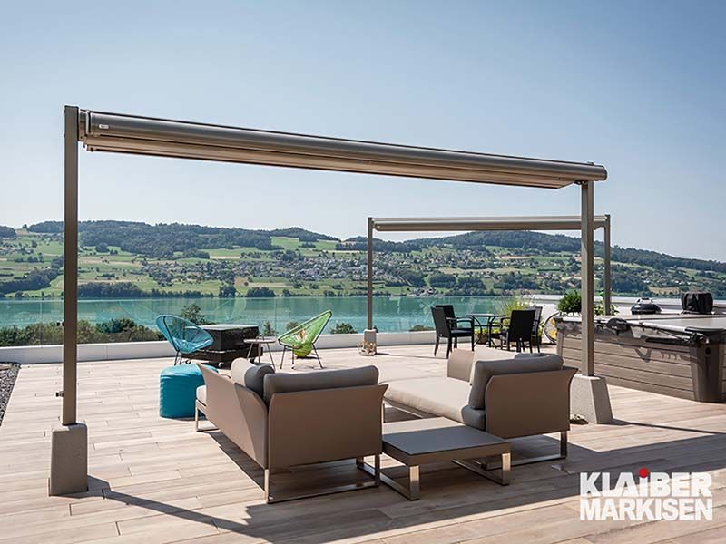 Eine Terrasse mit Sofa, Stühlen, Tischen und einem Baldachin mit Blick auf einen See.
