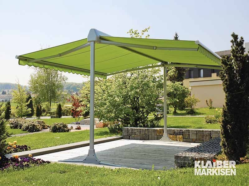 Eine grüne Markise steht auf einer Terrasse in einem Garten.