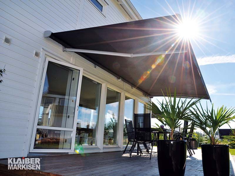 Ein weißes Haus mit einer schwarzen Markise über einer Terrasse.