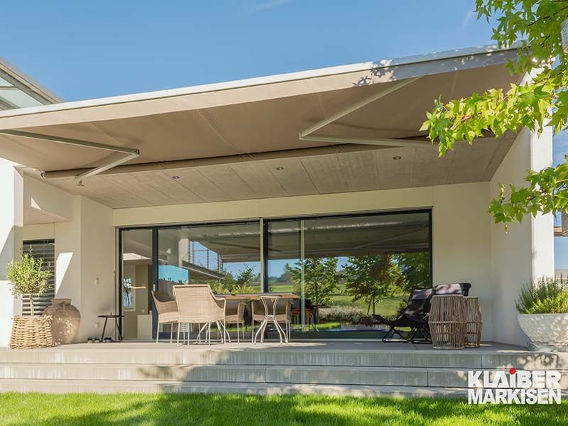 Ein großes weißes Haus mit einer Terrasse und einer großen Markise darüber.