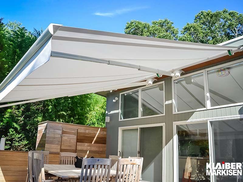 Eine weiße Markise überdacht eine Terrasse mit Tisch und Stühlen.