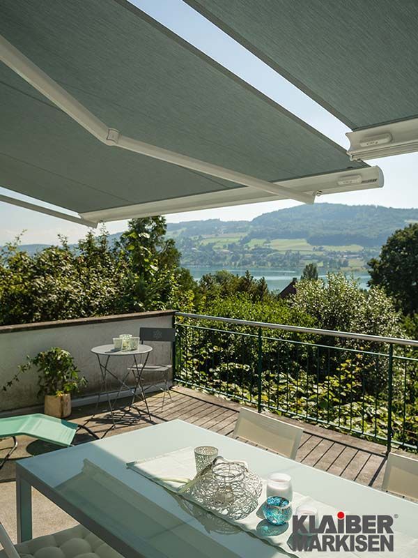 Ein Balkon mit Tisch und Stühlen unter einer Markise mit Blick auf einen See.