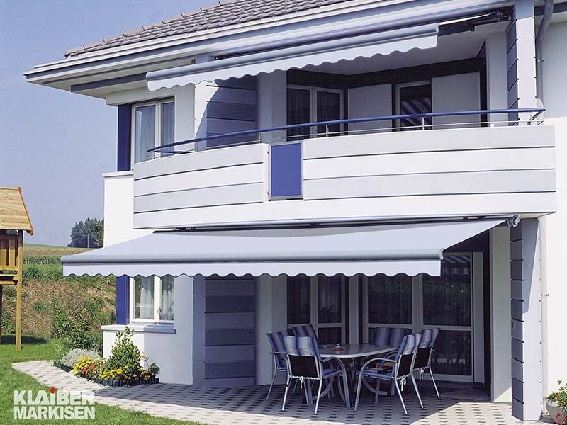 Ein weißes Haus mit einem blauen Balkon und einer weißen Markise