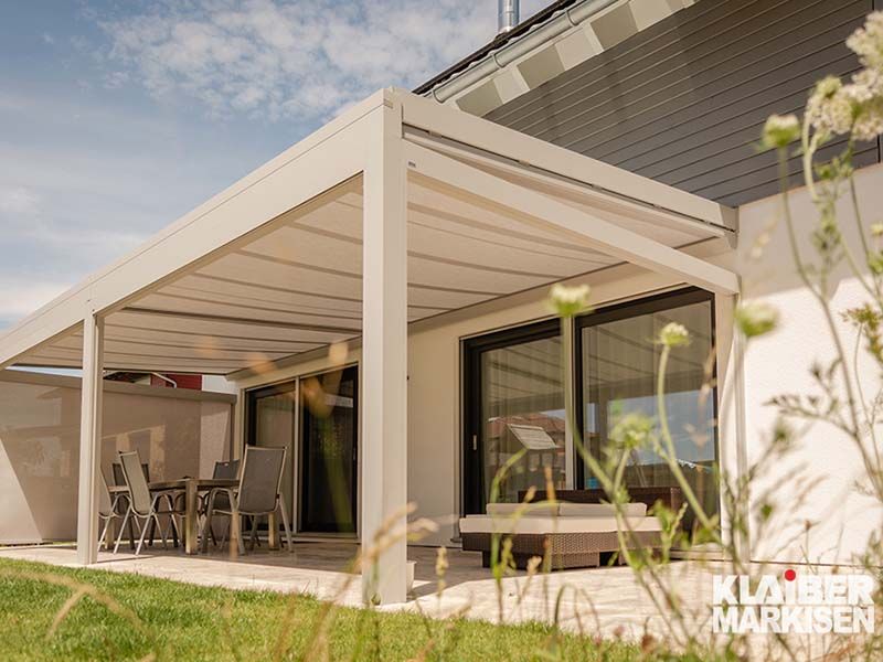 Eine weiße Pergola steht auf einer Terrasse neben einem Haus.
