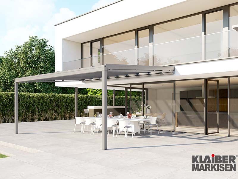 Ein großes weißes Haus mit einem großen Terrassenbereich mit Tischen und Stühlen unter einer Pergola.