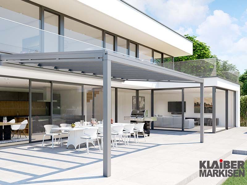 Ein großes weißes Haus mit einer Terrasse mit Tischen und Stühlen unter einer Pergola.