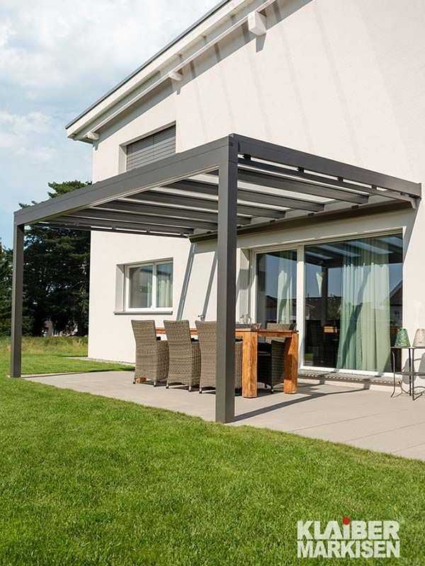 Eine Terrasse mit Pergola und Tisch und Stühlen vor einem Haus.