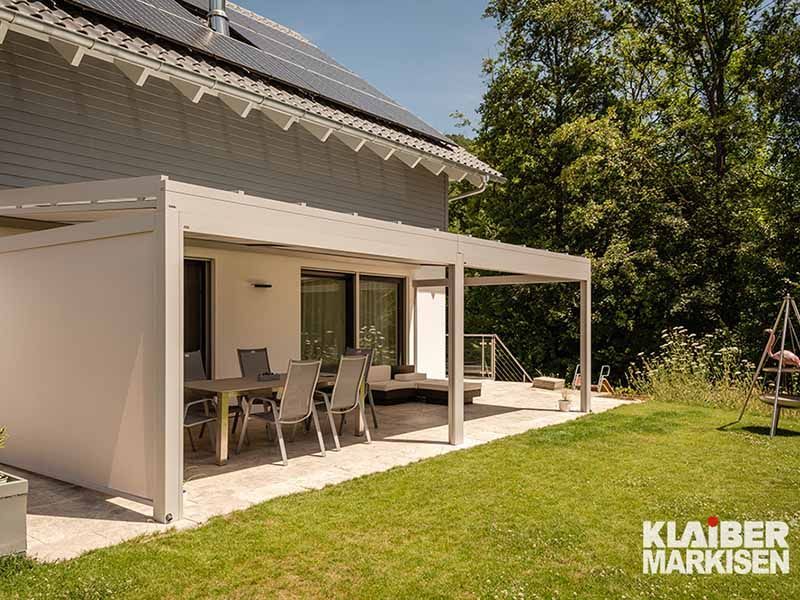 Ein weißes Haus mit einer überdachten Terrasse mit Tisch und Stühlen.